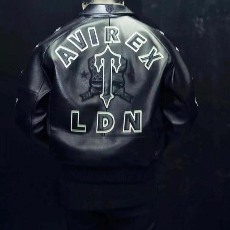 May include: Black leather jacket with white lettering spelling out "AVIREX" and "LDN". A central emblem features a stylized "T" design. The jacket has a classic bomber style.