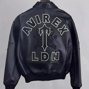May include: Black leather bomber jacket with white embroidered "AVIREX LDN" lettering and a stylized emblem on the back. The jacket features a classic bomber collar, ribbed cuffs, and a ribbed hem. A stylish outerwear piece.