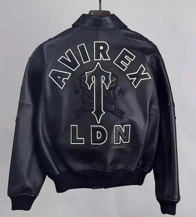 May include: Black leather bomber jacket with white embroidered "AVIREX LDN" lettering and a stylized emblem on the back. The jacket features a classic bomber collar, ribbed cuffs, and a ribbed hem. A stylish outerwear piece.