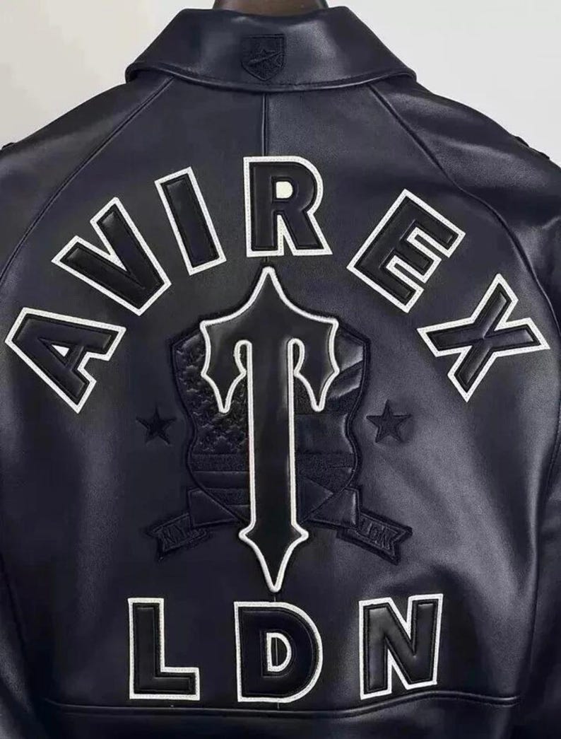 May include: Black leather jacket with white lettering and a shield emblem. The jacket features the word "AVIREX" across the top, a shield with a "T" design, and "LDN" at the bottom. Two stars flank the shield.