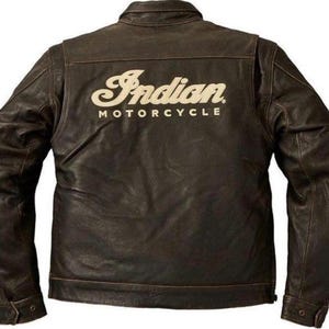 May include: A brown leather motorcycle jacket with the words "Indian MOTORCYCLE" in a cream-colored script across the back. The jacket has a classic design with a collar, buttoned cuffs, and a slightly distressed appearance.