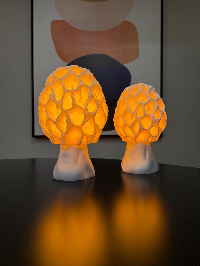 Puede incluir: Dos l&aacute;mparas con forma de seta con sombreretes blancos texturizados de patr&oacute;n de panal que emiten una luz naranja c&aacute;lida y brillante. Las l&aacute;mparas tienen bases blancas lisas y s&oacute;lidas, y se mantienen erguidas proyectando un suave resplandor &aacute;mbar.
