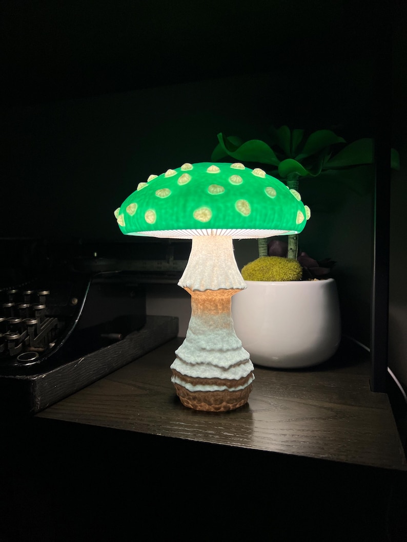 May include: A mushroom-shaped lamp featuring a vibrant green cap with raised, lighter-colored spots. The stem is textured with a white, ridged upper section that transitions into a brown, earthy base. The lamp emits a soft, warm glow from underneath.