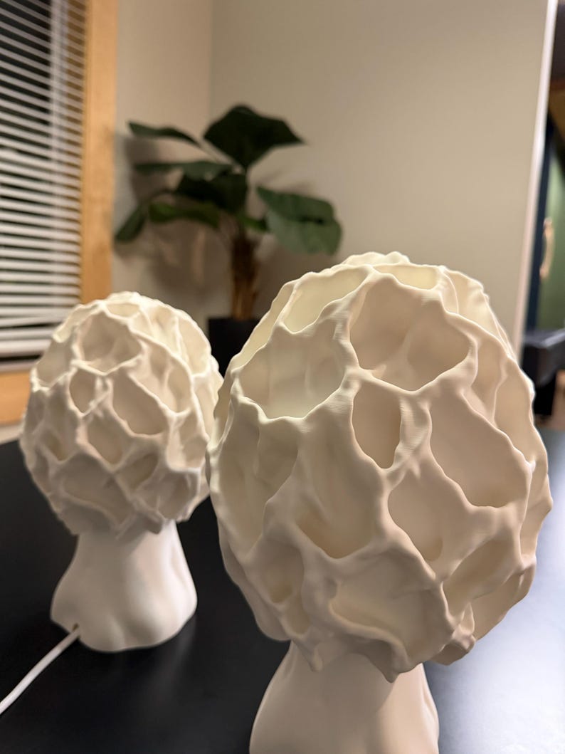 Puede incluir: Dos l&aacute;mparas de mesa blancas con un exterior texturizado, org&aacute;nico y similar a un panal. Cada l&aacute;mpara presenta una secci&oacute;n superior redondeada y bulbosa con hendiduras profundas e irregulares y una base lisa y c&oacute;nica.