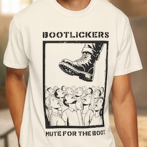 Peut inclure: T-shirt blanc avec un graphisme noir et blanc. Le graphisme représente une botte piétinant une foule, avec les mots "BOOTLICKERS" et "MUTE FOR THE BOOT" en lettres noires grasses.