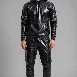 May include: A black, shiny, hooded tracksuit. The set includes a hooded sweatshirt with a front pocket and matching pants. The pants have pockets on the side and are cuffed at the ankles. The model is wearing black sneakers.