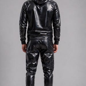 May include: A black, shiny tracksuit set. The set includes a hooded jacket and matching pants. The jacket has a zipper closure and the pants have pockets. The outfit is made of a glossy material and is worn with black sneakers.