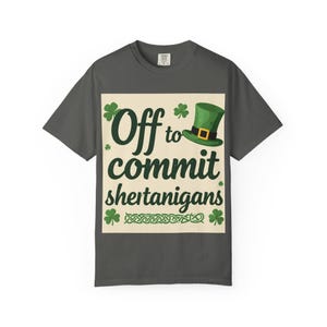 Può includere: T-shirt grigio scuro con grafica per la festa di San Patrizio. La grafica presenta il testo "Off to commit shertanigans" con un cappello da folletto verde e trifogli. La maglietta è a girocollo.