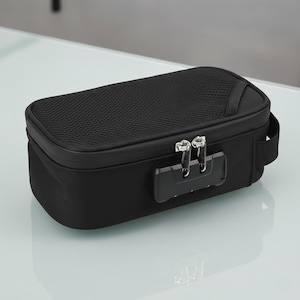 May include: A black rectangular storage bag with a mesh top and a combination lock. The bag has a zip closure and a small handle on the side. The bag is on a white surface.
