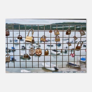 May include: A white ceramic mug with a black handle and the text "But First, Coffee" in a bold, black font. The mug is set against a blurred background, suggesting a cozy setting.