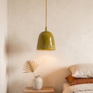Peut inclure: Une suspension en forme de dôme avec un abat-jour en céramique vert olive brillant présentant des indentations texturées verticales à la base. Le luminaire est suspendu par un cordon fin et possède un raccord métallique doré au sommet.