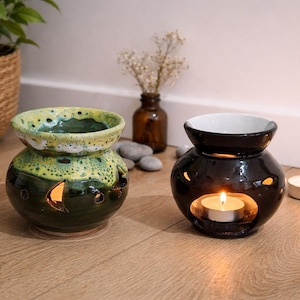 Peut inclure: Deux diffuseurs d'huiles essentielles en céramique, un vert et jaune, l'autre noir, avec des bougies allumées à l'intérieur. Le diffuseur vert a un motif tacheté. Le noir a une finition brillante.