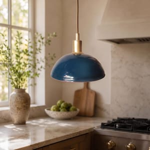 Peut inclure: Une suspension lumineuse en forme de dôme dotée d'un abat-jour bleu profond à la finition brillante et d'un connecteur supérieur cylindrique doré, suspendue par un cordon fin, conçue pour l'éclairage zénithal dans un espace cuisine.
