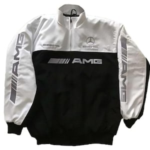Puede incluir: Chaqueta con cremallera negra y blanca con el logotipo de AMG en las mangas y el pecho. La chaqueta tiene un cuello alto y un logotipo de Mercedes-Benz. La chaqueta está hecha de un material ligero.