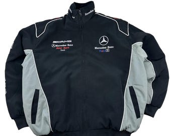 May include: Black and gray Mercedes-Benz racing jacket with white trim. Features the AMG Mercedes-Benz Motor Sport Team logo and the Mercedes-Benz Mobil 1 logo. Includes a full-length zipper and two front pockets.