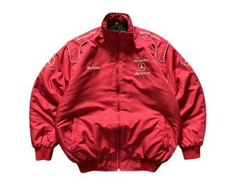 May include: A red bomber jacket with a full zipper closure. The jacket features white accents and the Mercedes-Benz logo on the chest and shoulders. The name "Mathias" is printed on the left chest.