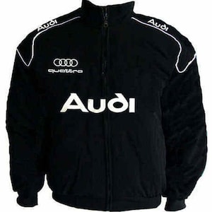 May include: Black zip-up jacket with white accents and the Audi logo prominently displayed. The jacket features the Audi logo on the chest, shoulders, and the word "quattro" below the logo. A sporty, casual outerwear item.