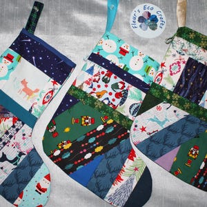 May include: Three quilted Christmas stockings featuring patchwork designs with various holiday-themed fabrics, including snowmen, nutcrackers, reindeer, and Santa Claus. Each stocking has a fabric hanging loop and a circular logo reading Fleur's Eco Crafts.