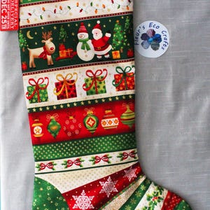 May include: A Christmas stocking featuring horizontal bands of holiday patterns including reindeer, a snowman, Santa Claus, wrapped gifts, and ornaments. The fabric displays red, green, and gold colours with a red tag labelled SPECIAL DELIVERY DO NOT OPEN UNTIL DEC 25TH.