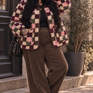 Könnte beinhalten: Eine braune Mütze mit dem Text "Rockes mit Liebe", eine langärmelige Jacke mit Karomuster aus cremefarbenen, braunen und rosafarbenen Blumenquadraten, ein schwarzes Oberteil, eine braune Cordhose mit weitem Bein, eine schwarze Handtasche und beige Plateauschuhe.