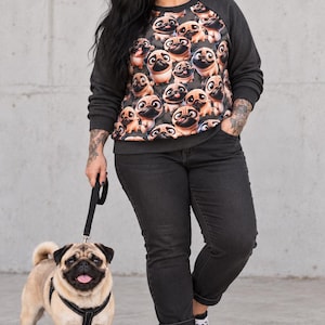 Könnte beinhalten: Ein langärmeliges Sweatshirt mit einem sich wiederholenden Muster aus Cartoon-Mops-Gesichtern auf der Vorderseite, kombiniert mit einer dunkelgrauen Jeans und schwarz-weißen Sneakern. Das Sweatshirt hat dunkelgraue Raglanärmel und einen Rundhalsausschnitt.
