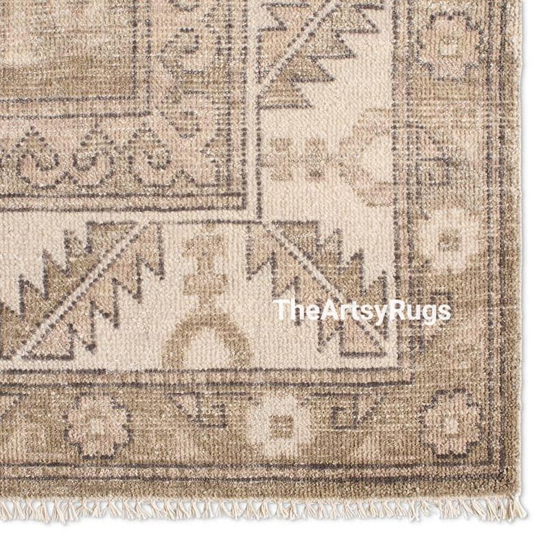 May include: Close-up of a beige and brown patterned rug with a fringe. The rug features geometric designs and the text "TheArtsyRugs". The rug has a vintage, distressed look.