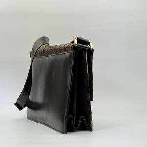 May include: A brown leather shoulder bag with a flap closure and a long strap. The bag features a textured, patterned panel and gold-tone hardware. The bag's design is classic and suitable for everyday use.