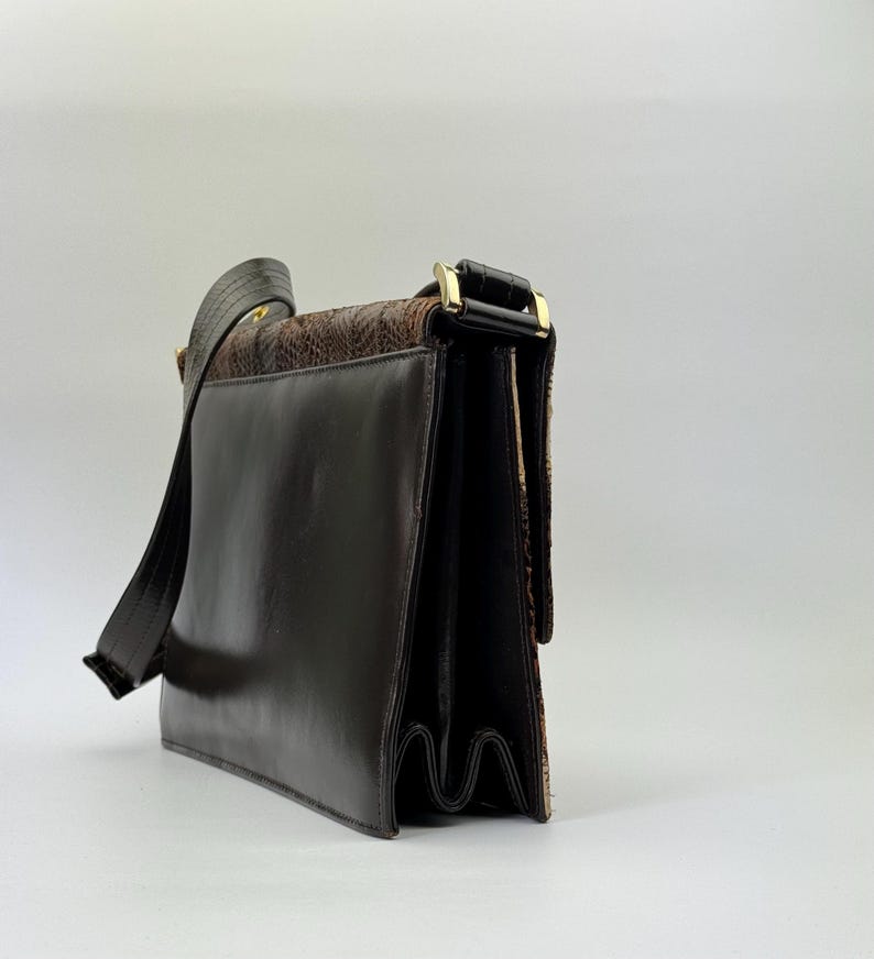 May include: A brown leather shoulder bag with a flap closure and a long strap. The bag features a textured, patterned panel and gold-tone hardware. The bag's design is classic and suitable for everyday use.