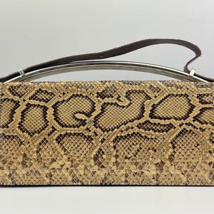 Può includere: Borsa rettangolare con motivo a pelle di serpente nei toni del beige e del marrone. Presenta un manico argentato e un cinturino in pelle marrone scuro. Un accessorio elegante.
