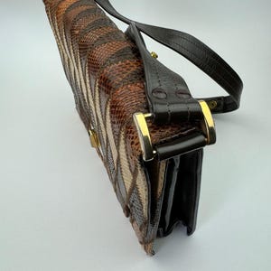 May include: A vintage handbag with a snakeskin pattern in shades of brown, tan, and black. The bag features a black leather strap and gold-colored hardware. The bag is rectangular and has a clasp closure.