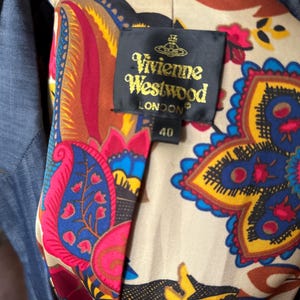 May include: A blue blazer with a beige lining featuring a colorful paisley pattern in red, yellow, blue, and black. A black label is sewn into the lining with the gold text Vivienne Westwood LONDON and the number 40 printed below the brand name.