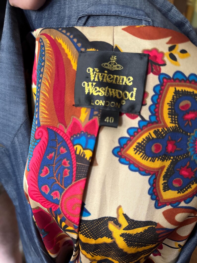 May include: A blue blazer with a beige lining featuring a colorful paisley pattern in red, yellow, blue, and black. A black label is sewn into the lining with the gold text Vivienne Westwood LONDON and the number 40 printed below the brand name.