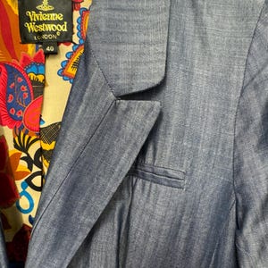May include: A blue blazer with a notched lapel and a welt pocket on the chest. The interior lining features a colorful paisley pattern in red, yellow, and blue. A black label with gold text reads Vivienne Westwood London and the number 40.