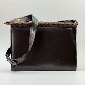 May include: A dark brown leather shoulder bag with a rectangular shape. The top section features a snakeskin pattern in shades of brown. The bag has a long, dark brown strap and metal hardware.