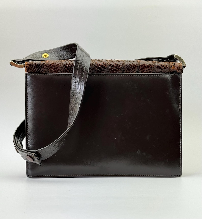 May include: A dark brown leather shoulder bag with a rectangular shape. The top section features a snakeskin pattern in shades of brown. The bag has a long, dark brown strap and metal hardware.
