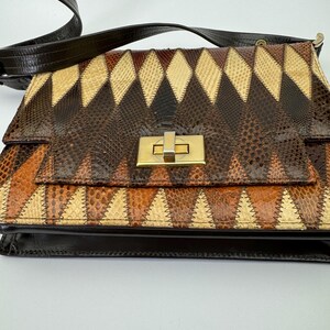 May include: A vintage shoulder bag with a geometric pattern. The bag features a patchwork design in shades of brown, tan, and cream, with a gold-tone clasp. The strap is dark brown.