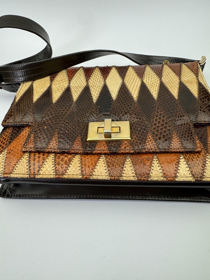 May include: A vintage shoulder bag with a geometric pattern. The bag features a patchwork design in shades of brown, tan, and cream, with a gold-tone clasp. The strap is dark brown.