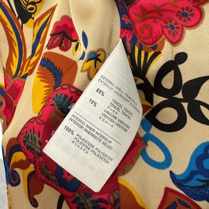 May include: A garment interior featuring a vibrant floral pattern in shades of red, yellow, blue, and black on a beige background. A white care label is attached, listing 85% Tencel, 15% Viscose for the shell, and 100% Polyester for the inner lining.