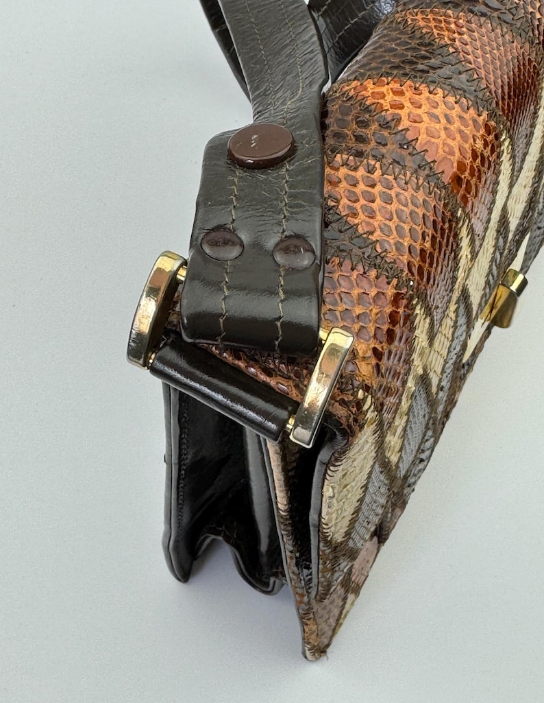 May include: A vintage handbag with a patchwork design. The bag features a mix of brown, tan, and cream-colored panels with a snakeskin pattern. It has a dark brown leather strap and gold-colored hardware.