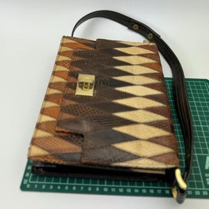 May include: A brown and tan patterned handbag with a dark brown strap. The bag features a geometric design and a gold-colored clasp. The strap is attached with gold-colored hardware.