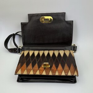 May include: Open, vintage handbag with a geometric pattern. The flap is open, revealing a diamond pattern in shades of brown, tan, and black. The bag has a black leather exterior and a gold-tone clasp. A black shoulder strap is attached.
