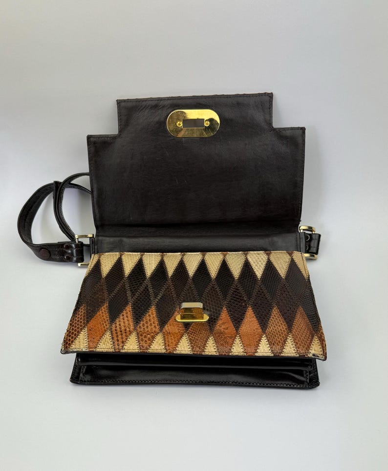 May include: Open, vintage handbag with a geometric pattern. The flap is open, revealing a diamond pattern in shades of brown, tan, and black. The bag has a black leather exterior and a gold-tone clasp. A black shoulder strap is attached.