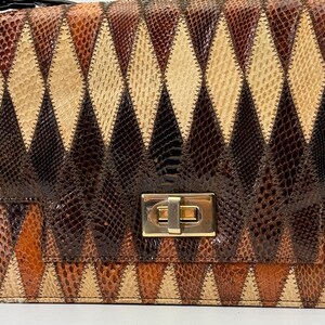 May include: A rectangular handbag with a geometric diamond pattern in shades of brown, tan, and black. The bag features a gold-colored clasp and a black strap. The design resembles a patchwork or quilt, with each diamond segment stitched together.