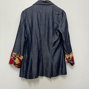 May include: A dark blue blazer with a notched collar and long sleeves. The sleeve cuffs are turned up to reveal a beige lining featuring a vibrant, multi-colored floral pattern in shades of red, blue, yellow, and green against a cream background.