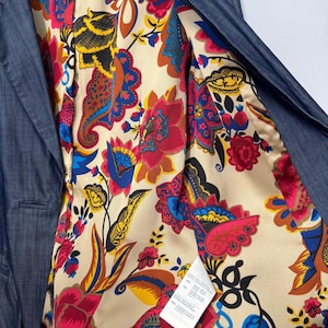 May include: A dark blue blazer with a vibrant, multicolored floral and paisley print lining. The interior features a Vivienne Westwood London label and a white care tag. The fabric has a subtle texture, and the lining displays bold red, yellow, and blue patterns on a cream background.