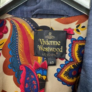 May include: A blue denim jacket featuring a vibrant, multicolored paisley print lining in shades of red, yellow, and blue. A black fabric label is stitched inside, displaying the text Vivienne Westwood London and the number 40.