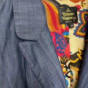 May include: A blue blazer with a notched lapel and a vibrant, multicolored paisley print lining. A black label inside the collar features the text Vivienne Westwood London and the number 40. The outer fabric has a subtle, fine-textured weave.