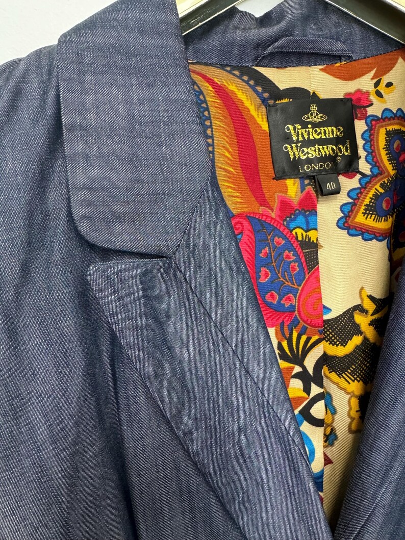 May include: A blue blazer with a notched lapel and a vibrant, multicolored paisley print lining. A black label inside the collar features the text Vivienne Westwood London and the number 40. The outer fabric has a subtle, fine-textured weave.