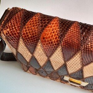 May include: A vintage handbag with a patchwork design. The bag features a variety of brown, tan, and black diamond-shaped patches, creating a textured surface. It has a brown leather strap and a gold-toned clasp.