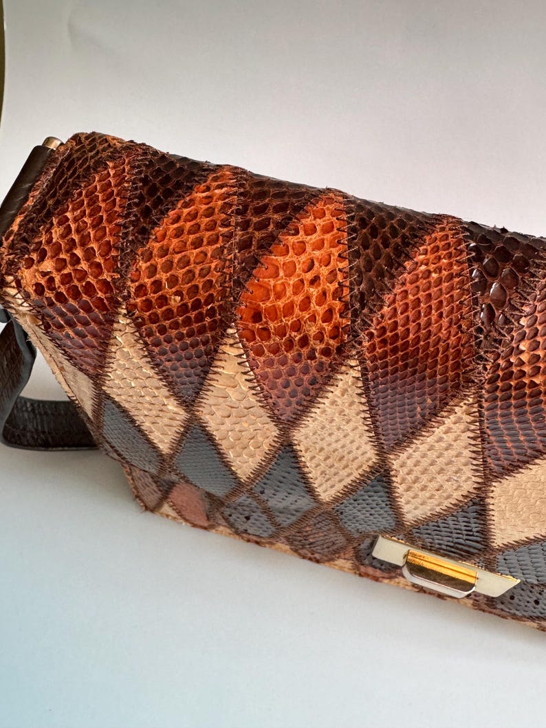 May include: A vintage handbag with a patchwork design. The bag features a variety of brown, tan, and black diamond-shaped patches, creating a textured surface. It has a brown leather strap and a gold-toned clasp.